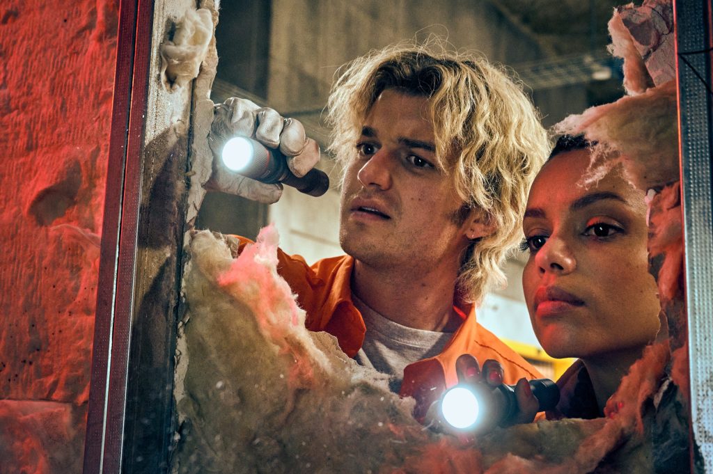 Joe Keery and Georgina Campbell shining torches through a hole in the film Cold Storage.