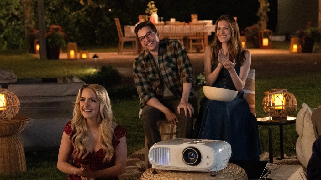 McKenna Grace, Dave Franco and Allison Williams smiling and watching a film outside using a projector, in the film Regretting You.