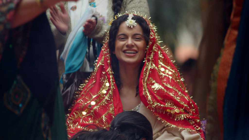 Kangana Ranaut smiling and wearing a red headscarf in the film Queen.